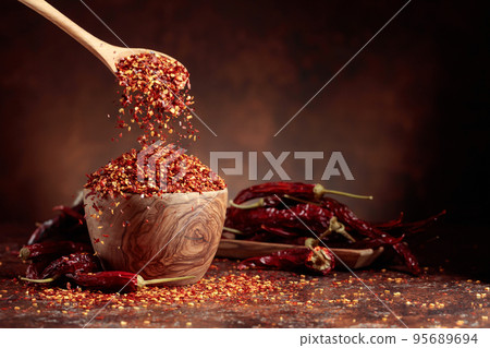 Chilli flakes are poured into a wooden dish. 95689694