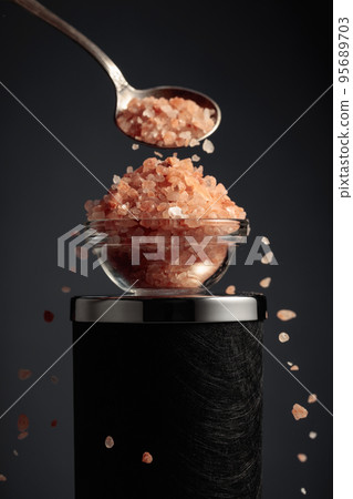 Pink salt is poured into a small bowl. 95689703