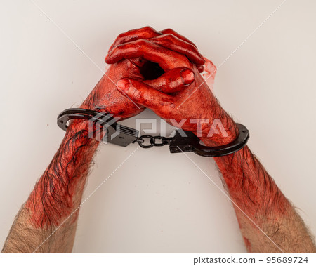 Bloodied male hands in handcuffs, folded on a white table. Bloodied male hands in handcuffs, folded on a white table. 95689724