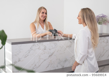 A young woman pays in a beauty salon with a credit card using NFC contactless payment. A young woman pays in a beauty salon with a credit card using NFC contactless payment. 95689914