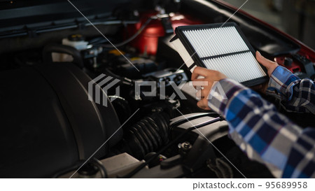 Caucasian female auto mechanic changes the engine air filter in the car. 95689958