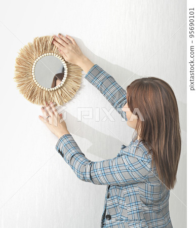 Decorator hanging mirror on white wall in room. Interior designer decorating wall in boho style. vertical. Decorator hanging mirror on white wall in room. Interior designer decorating wall in boho style. vertical. 95690101