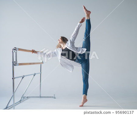 Caucasian woman in casual clothes pulls the split at the ballet barre. Caucasian woman in casual clothes pulls the split at the ballet barre. 95690137