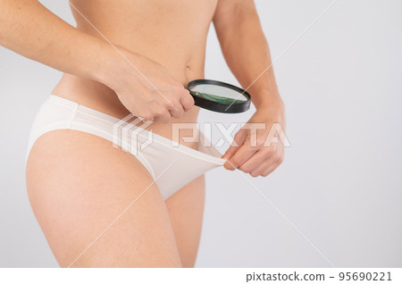 A woman in white shorts looks at the pubis through a magnifying glass on a white background. A woman in white shorts looks at the pubis through a magnifying glass on a white background. 95690221
