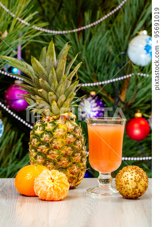 Pineapple, a glass of juice and a fir tree with Christmas ornaments. 95691019