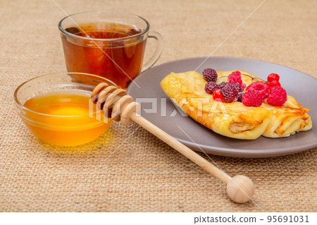 Homemade pancakes with honey in a bowl and a cup of tea 95691031