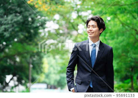 Young businessman walking in green Young businessman walking in green 95691133