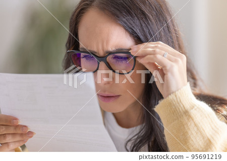 The woman has vision problems and reads the letter very close to her eyes and glasses 95691219