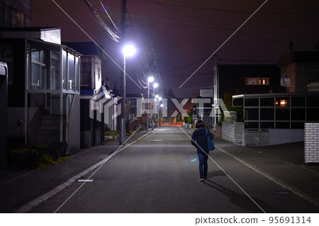 A woman walking on a street in a residential area at night A woman walking on a street in a residential area at night 95691314