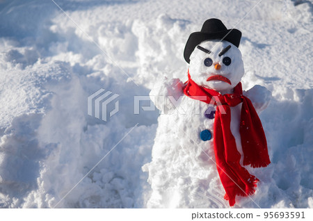 A snowman with a creepy grimace in a hat and scarf. 95693591