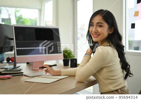 Beautiful young female photo editor sitting in creative workplace and retouching photos on computer 95694314