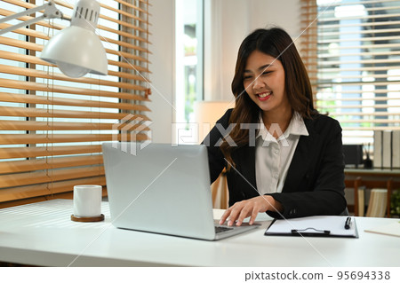 Pleasant young business woman communicating in social network, searching information online on laptop computer 95694338