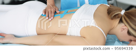 Doctor examine x ray of womans back, put kinesiology tape on ache part of body 95694339