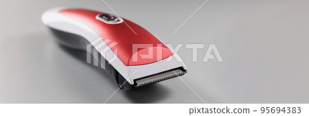 Electric trimming machine for hair, device with red colour design on grey surface Electric trimming machine for hair, device with red colour design on grey surface 95694383