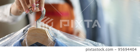 Worker giving to client clean clothes hanging on hangers at dry cleaning company 95694404
