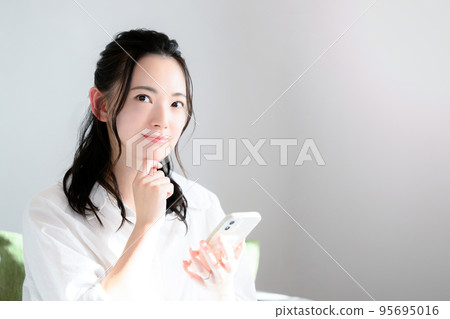 A cute woman thinking with her smartphone 95695016