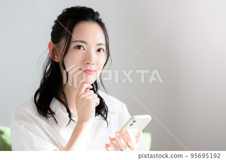 A cute woman thinking with her smartphone A cute woman thinking with her smartphone 95695192