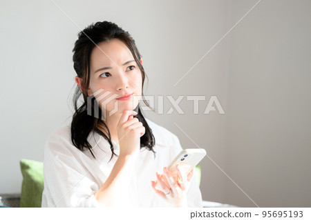 A cute woman thinking with her smartphone 95695193
