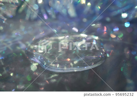 A drop of serum in tinsel in a Christmas theme in purple shades in dark tones. A drop of serum in tinsel in a Christmas theme in purple shades in dark tones. 95695232