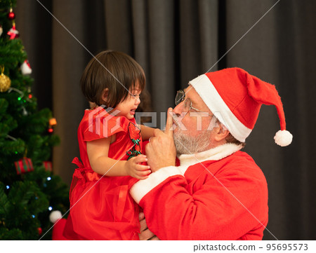Side view of Santa Claus comforts crying kid little girl at home. 95695573