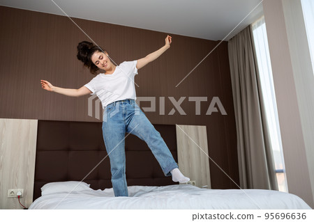 Happy young caucasian woman having fun and dancing on the bed in the bedroom. Bottom view Happy young caucasian woman having fun and dancing on the bed in the bedroom. Bottom view 95696636