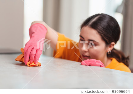 Blurred portrait of a young woman in rubber gloves is busily wiping the table with a rag. Close-up. House cleaning 95696664