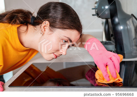 Housework. Portrait of a housewife in rubber gloves diligently wiping an induction cooker with a rag Housework. Portrait of a housewife in rubber gloves diligently wiping an induction cooker with a rag 95696668