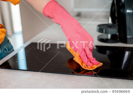 Cleaning the house. A cleaner in rubber gloves wipes the cooking surface with a rag. Hands close up Cleaning the house. A cleaner in rubber gloves wipes the cooking surface with a rag. Hands close up 95696669