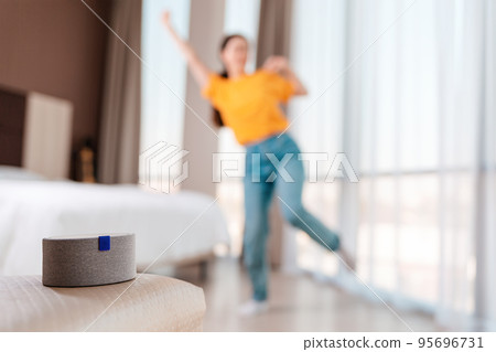 A portable smart gray speaker plays music. In the background, a woman dances in a blur. The concept of modern gadgets and entertaiment 95696731