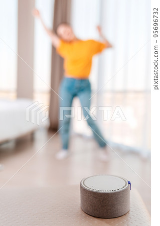 A portable smart speaker plays music. In the background, a woman dances in a blur. Vertical. The concept of modern gadgets 95696732