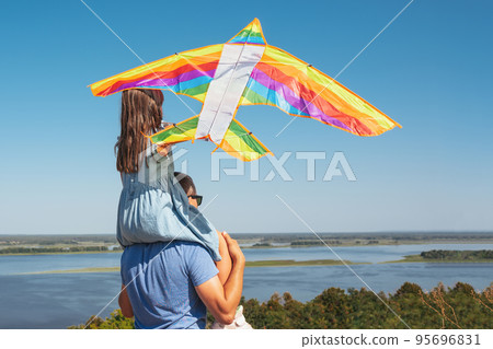 Happy child sits on his fathers shoulders with a kite in nature. View from the back 95696831