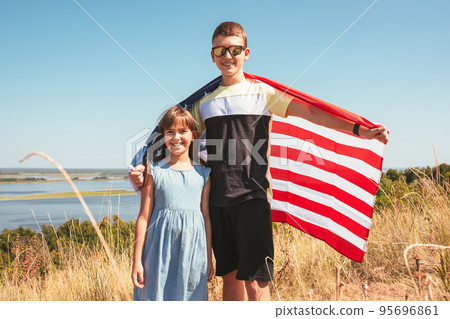 Two happy children with the flag of America in nature on a sunny day. Two happy children with the flag of America in nature on a sunny day. 95696861
