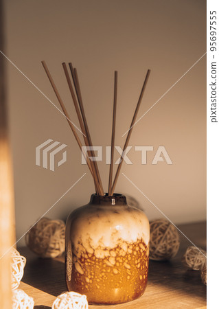 Cozy home decorations aroma reed diffuser in the living room. Home comfort concept. Bottle container with wood stick diffusers Essential oils to scent your home Minimalist air freshener concept. 95697555