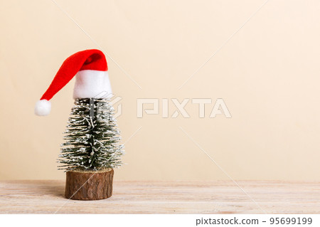 One small Christmas tree with santa hat on colored background. new year decoration with copy space One small Christmas tree with santa hat on colored background. new year decoration with copy space 95699199