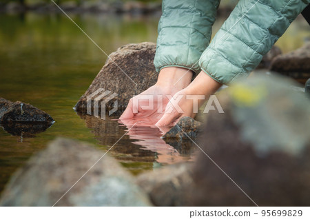 Close-up of water drops falling from female hands into a stream. The hand touches fresh water. A tourist drinks water from a reservoir in the mountains in summer on a sunny day 95699829