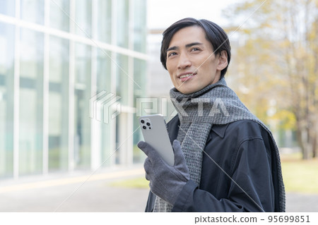 Portrait of a man wearing a scarf and gloves and holding a smartphone Portrait of a man wearing a scarf and gloves and holding a smartphone 95699851