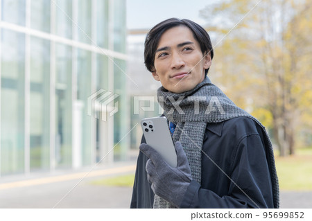 Portrait of a man wearing a scarf and gloves and holding a smartphone Portrait of a man wearing a scarf and gloves and holding a smartphone 95699852