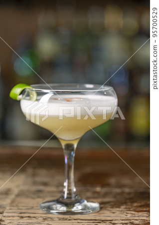 Vanilla Sour cocktail with egg white and lemon juice on the bar. Blurred background. Vanilla Sour cocktail with egg white and lemon juice on the bar. Blurred background. 95700529