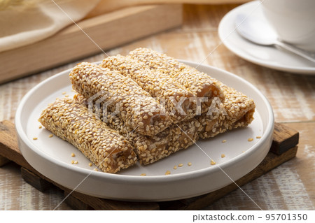 Golden brown roasted sesame seeds and peanuts are bound together by sugar to form delicious sesame bars,Thai snacks,Sesame Roll on white plate Golden brown roasted sesame seeds and peanuts are bound together by sugar to form delicious sesame bars,Thai snacks,Sesame Roll on white plate 95701350