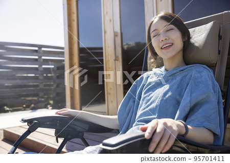 Sauna girls wearing a sauna poncho and taking an open air bath in front of an outdoor sauna 95701411