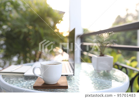 Laptop side view and white coffee cup with notebooks on white glass table outdoor balcony Laptop side view and white coffee cup with notebooks on white glass table outdoor balcony 95701483
