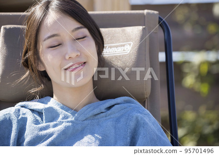Sauna girls wearing a sauna poncho and taking an open air bath in front of an outdoor sauna 95701496
