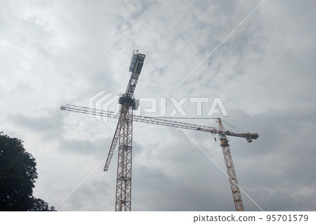 Against the background of a dark sky, tall tower cranes during construction. Against the background of a dark sky, tall tower cranes during construction. 95701579