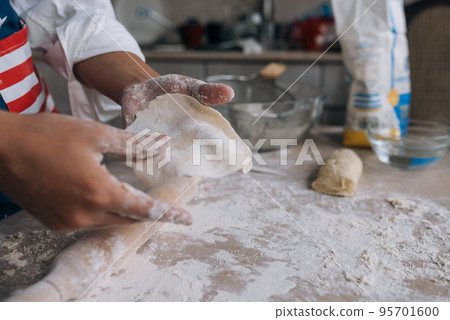 Young housewife in an apron kneads dough with her hands. 95701600