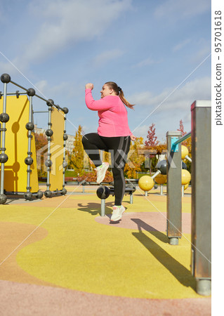 Outdoor training. Weight lost concept. Young woman doing fitness exercises at street public sports ground. Sunny autumn day. Sport, health, plans, body positive 95701618