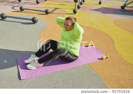 Outdoor training. Weight lost concept. Young woman doing fitness exercises at street public sports ground. Sunny autumn day. Sport, health, plans, body positive 95701626