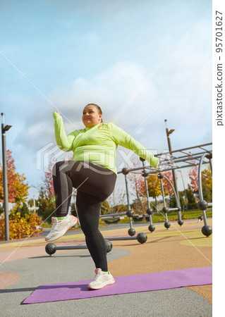 Energetic obese young woman in warm sportswear workout at sportsground in spring sunny day. Concept of challenges, dreams, fitness, healthy lifestyle 95701627