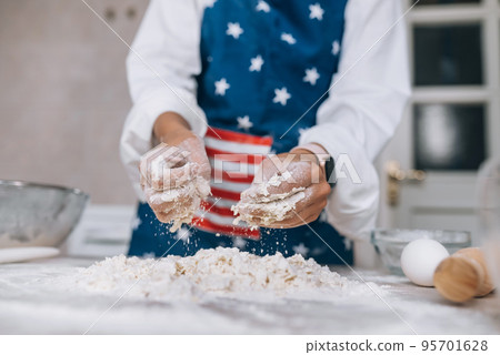 Young housewife in an apron kneads dough with her hands. Young housewife in an apron kneads dough with her hands. 95701628