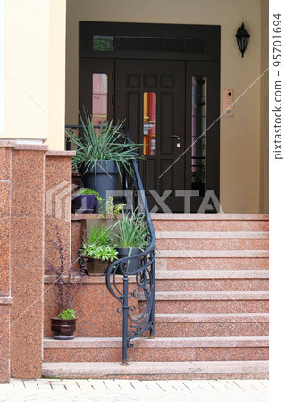 Pots of flowers and plants stand on the steps at the entrance to the house. Residential porch design. 95701694