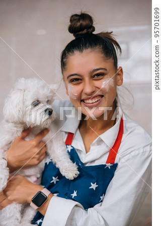 Smiling woman in kitchen holding cute white Maltese dog 95701699